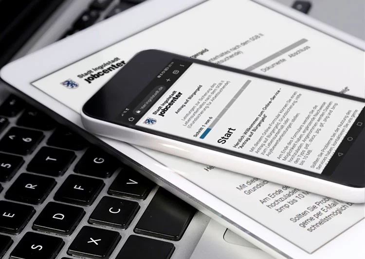 Selbst ist die Verwaltung: Onlineanträge im kommunalen Jobcenter 10 Digitalisierung in der öffentlichen Verwaltung – Smartphone und Tablet mit Online-Formular des Jobcenters auf Laptop-Tastatur, symbolisch für E-Government und digitale Services.