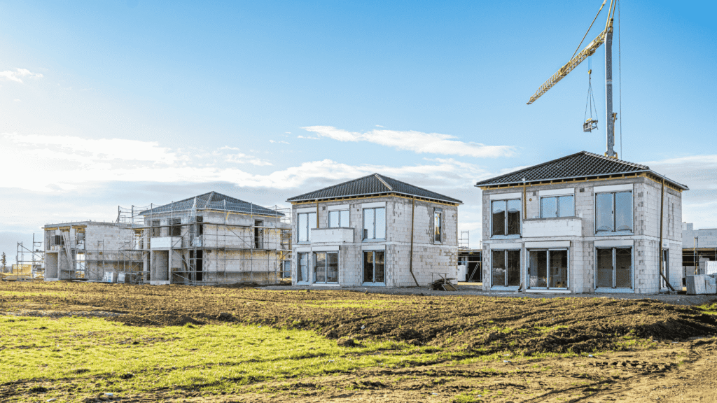Neubaugebiet mit Häusern im Rohbau und Baukran unter blauem Himmel